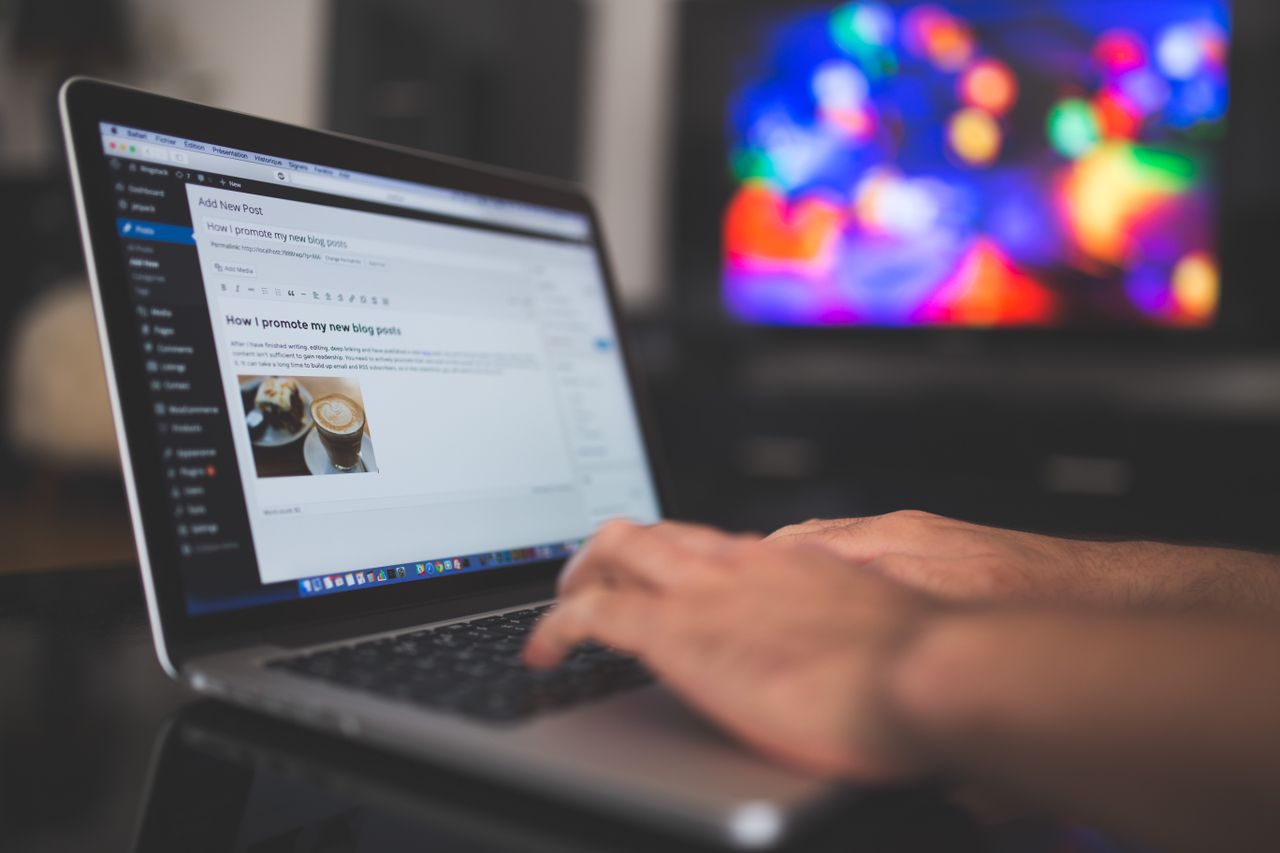 About Hands typing on a laptop with a blog post visible, cozy indoor setting with colorful screen in background.